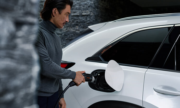 Un conducteur s’approche d’une Mazda avec un chargeur de niveau 2 à la main.