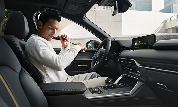 Man buckles his seatbelt in the driver’s seat of a parked CX-70.