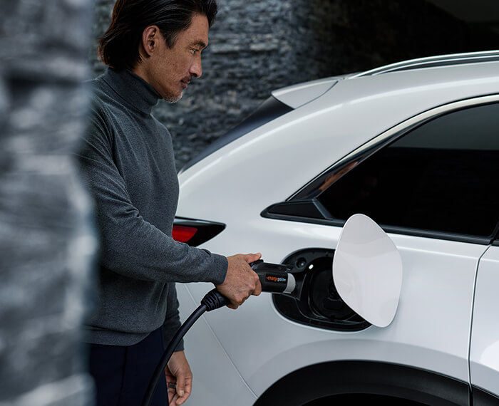 Un conducteur s’approche d’une Mazda avec un chargeur de niveau 2 à la main.