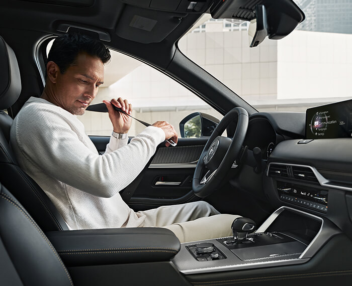 Man buckles his seatbelt in the driver’s seat of a parked CX-70.