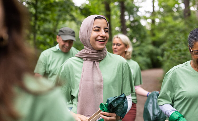 Smiling community members in nature wear matching green shirts while volunteering.