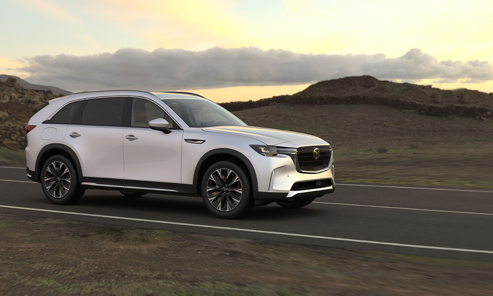 A white Mazda drives down a road alongside rocky terrain. 