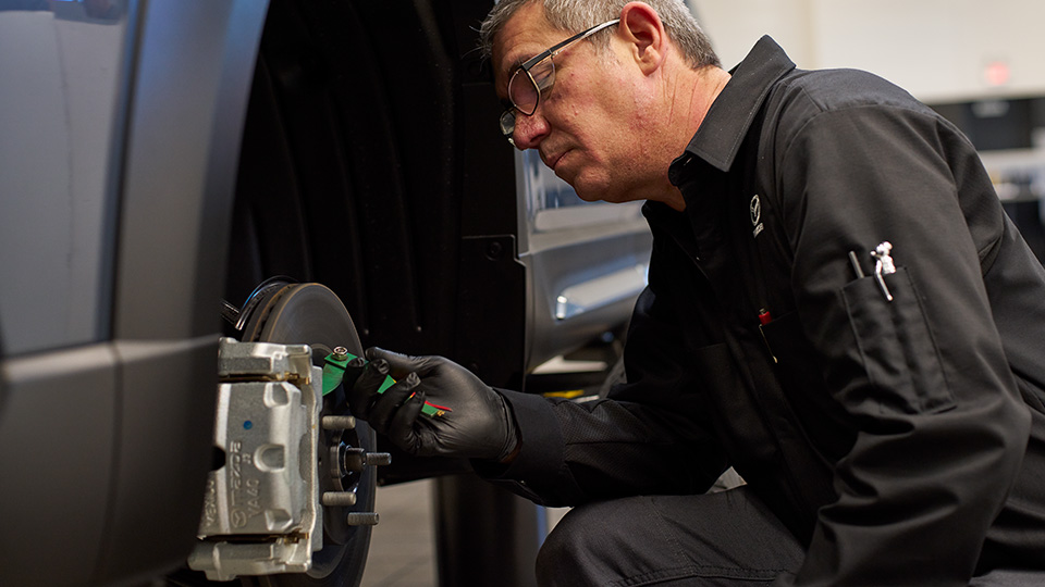 A Mazda technician working on a vehicle's brakes