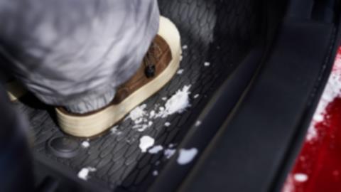 A close up image of a floor mat inside a vehicle with a snowy boot on it