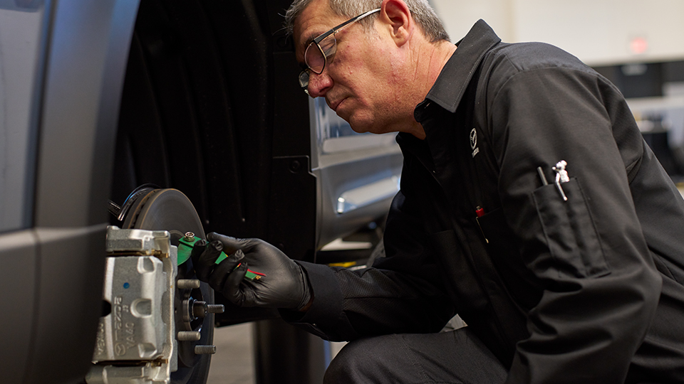 A Mazda technician working on a vehicle's brakes