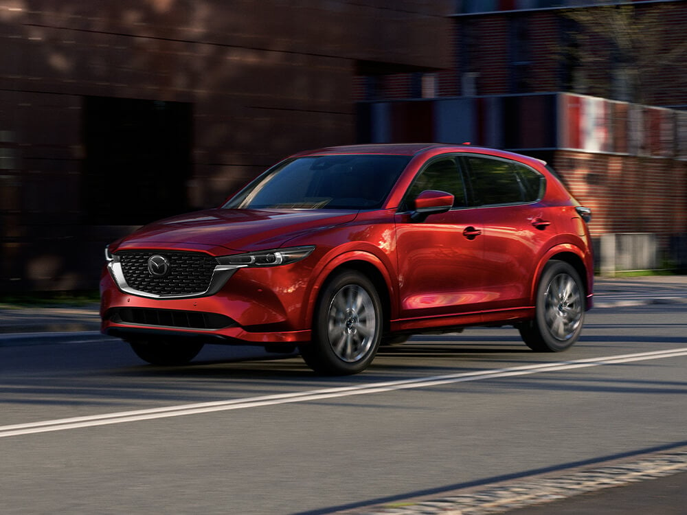 Red Mazda SUV turning corner on cobblestone street