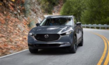 Machine Grey Metallic Mazda CX-30 takes a slight turn on an escarpment road. 