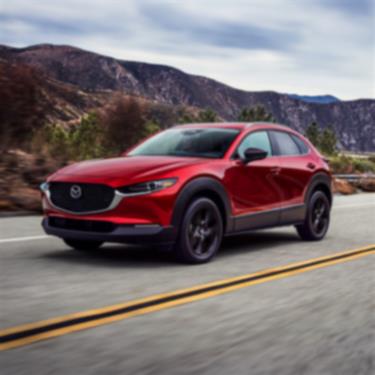 Soul Red Crystal Metallic Mazda CX-30 drives along mountainous highway. 