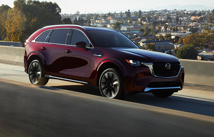 Artisan Red CX-90 driving down concrete highway overpass.