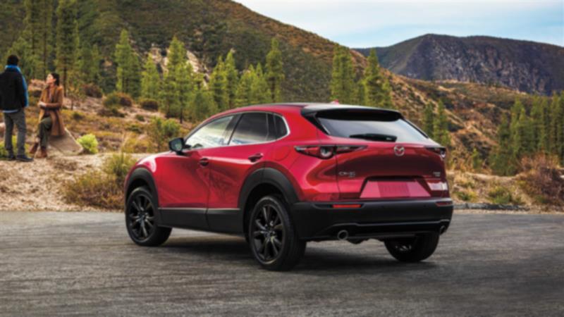 Back ¾ shot of Soul Red Crystal Metallic CX-30 parked roadside, mountains and trees in background. 