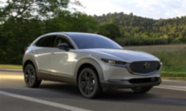 Front ¾ shot of Aero Grey Metallic CX-30 parked on shoulder of road, field and trees in background. 