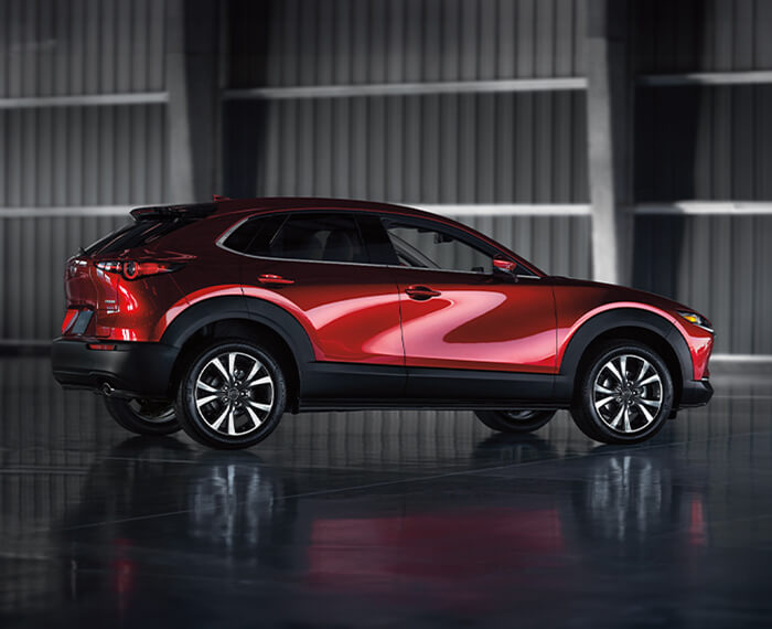 Passenger’s side profile of Soul Red Crystal Metallic CX-30 parked in stylish minimal warehouse environment. 