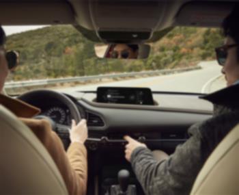 CX-30 driving on mountain road, view from inside, backseat looking forward at the driver and passenger in front seats.