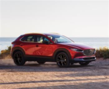 Soul Red Crystal Metallic Mazda CX-30 parked dirt road overlooking large lake in background.