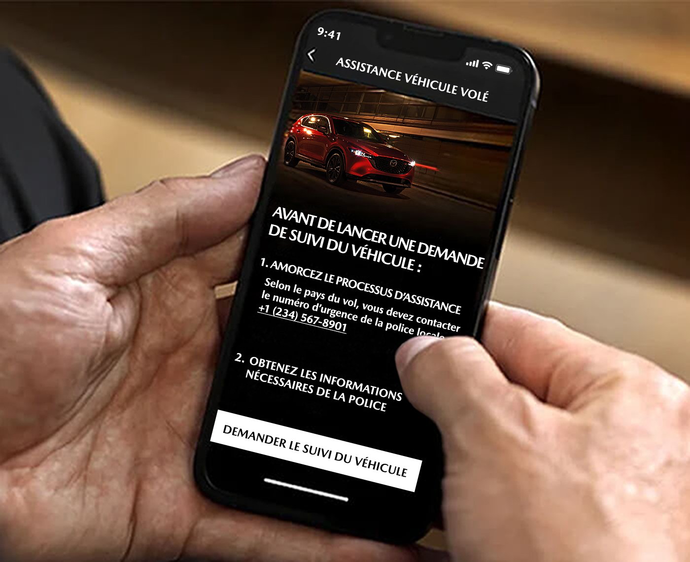 Des mains tiennent un téléphone intelligent affichant le suivi de véhicule volé de Mazda à l’écran.