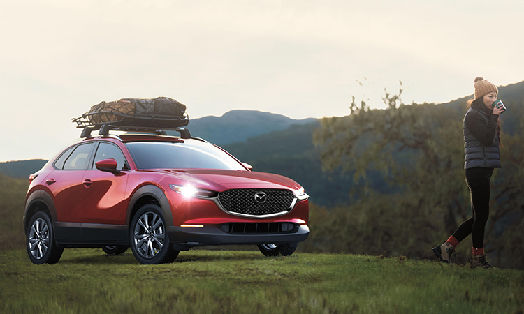 Un couple discute derrière leur CX-30 dont le hayon est ouvert. Des sacs de sport, une glacière et d’autres articles remplissent l’espace de chargement.