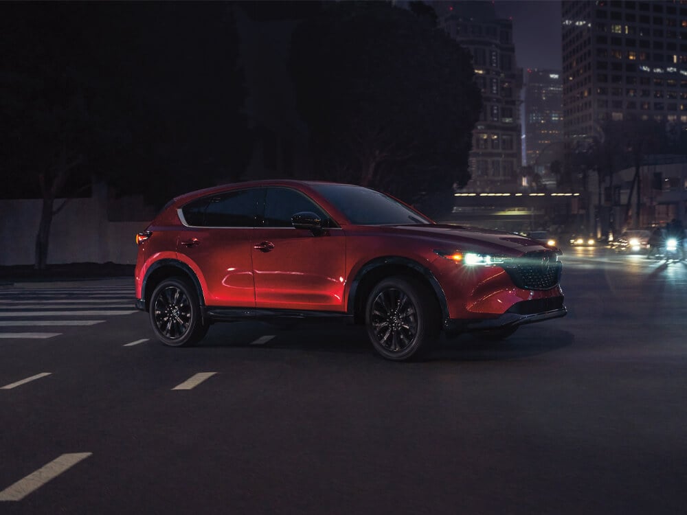 Un Mazda CX-5 rouge vibrant cristal métallisé avec le Groupe design sportif circule dans une rue. 