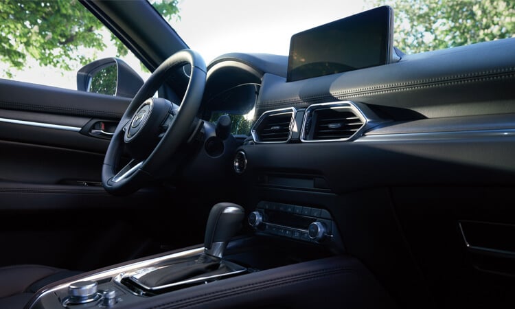 Vue en contre-plongée du volant, de la planche de bord, de l’écran et de la console d’un CX-5 depuis le siège passager. 