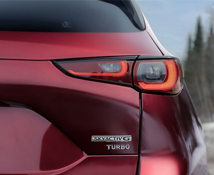 Gros plan de l’emblème Skyactiv G Turbo sur le hayon d’un Mazda CX-5 rouge vibrant cristal métallisé. 