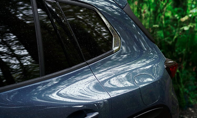 Close up of rear driver’s side panel of Ingot Blue Metallic Mazda CX-50, dense forest in background.