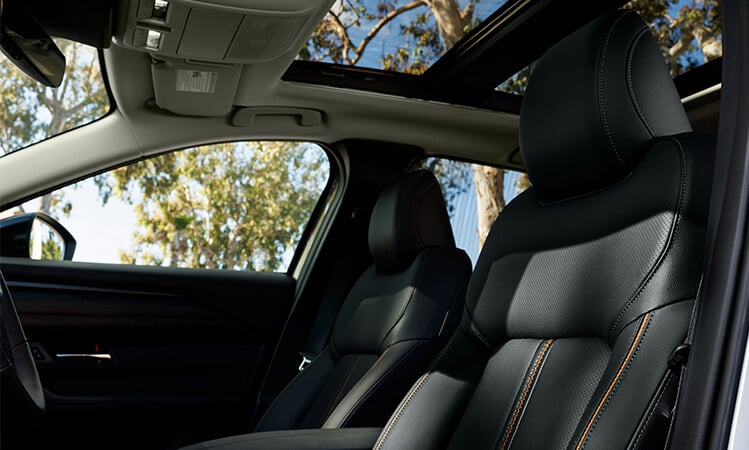 Low driver’s side view into Mazda CX-50 Hybrid interior showcasing black leather front seats with orange stitching. 