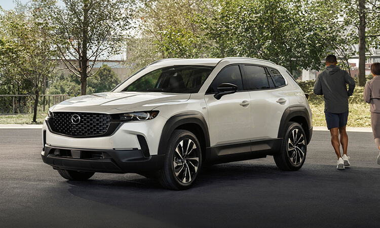 CX-50 Hybrid parked front ¾ in residential area. A man and woman are going for jog passing the rear of the vehicle.