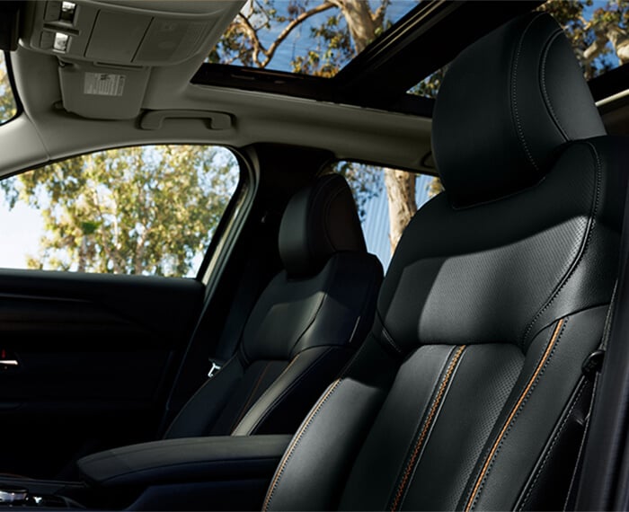 Low driver’s side view into Mazda CX-50 Hybrid interior showcasing black leather front seats with orange stitching.