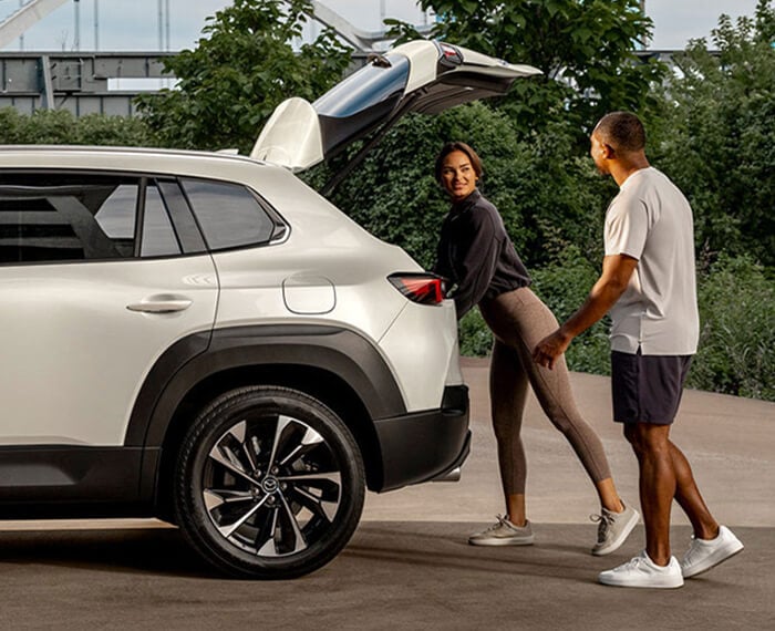 Profile view of CX-50 Hybrid with liftgate open, a man and a woman are at the rear, the woman is reaching in the cargo hold.