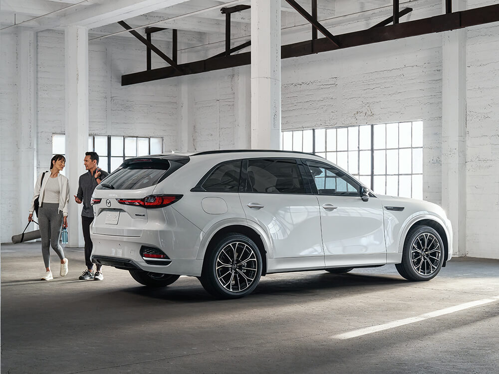 Couple with yoga gear chat in all-white, brick parking structure next to their CX-70 PHEV.