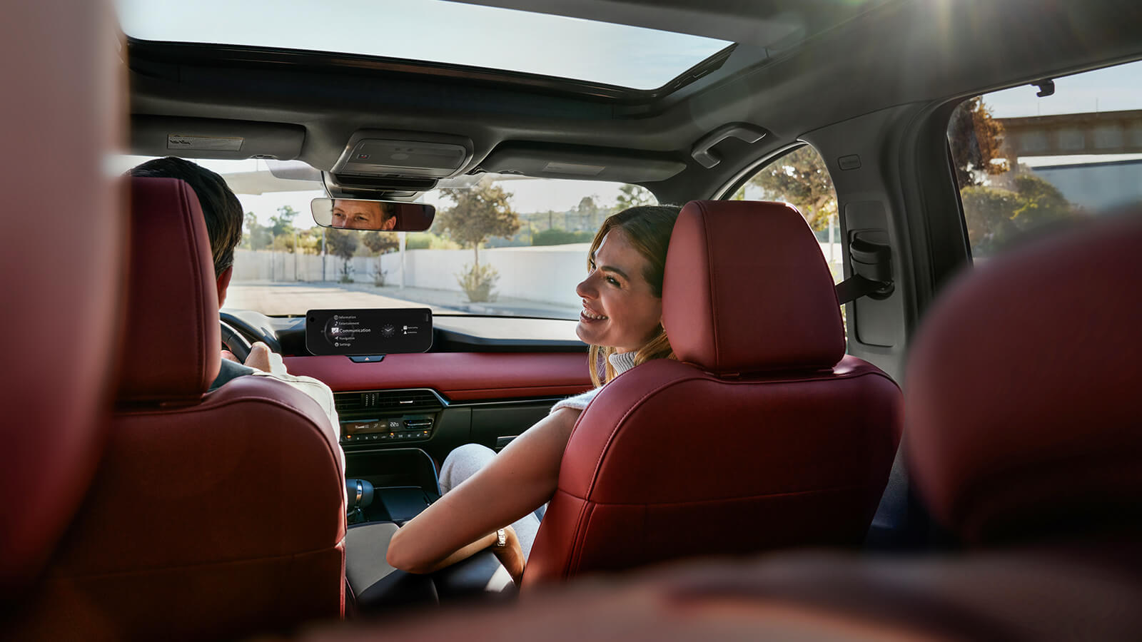 Shot from behind the second row inside the CX-70, the driver backs into a parking space while the passenger looks back with a smile.