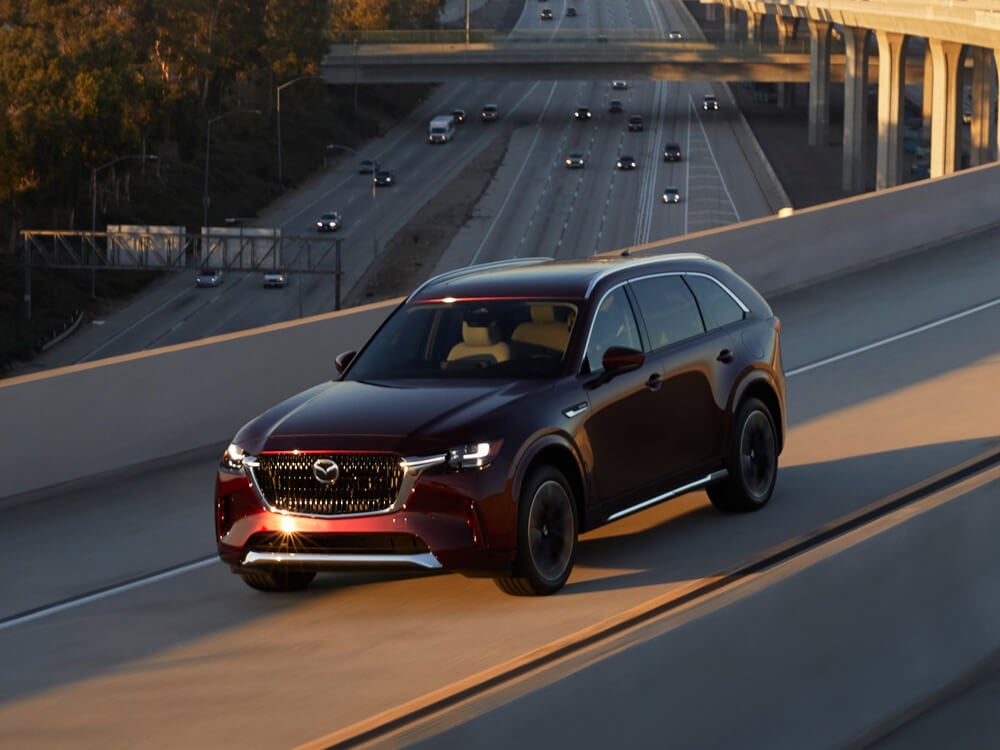 Un VÉHR CX-90 rouge artisan roule vers le coucher du soleil sur un pont autoroutier en béton.