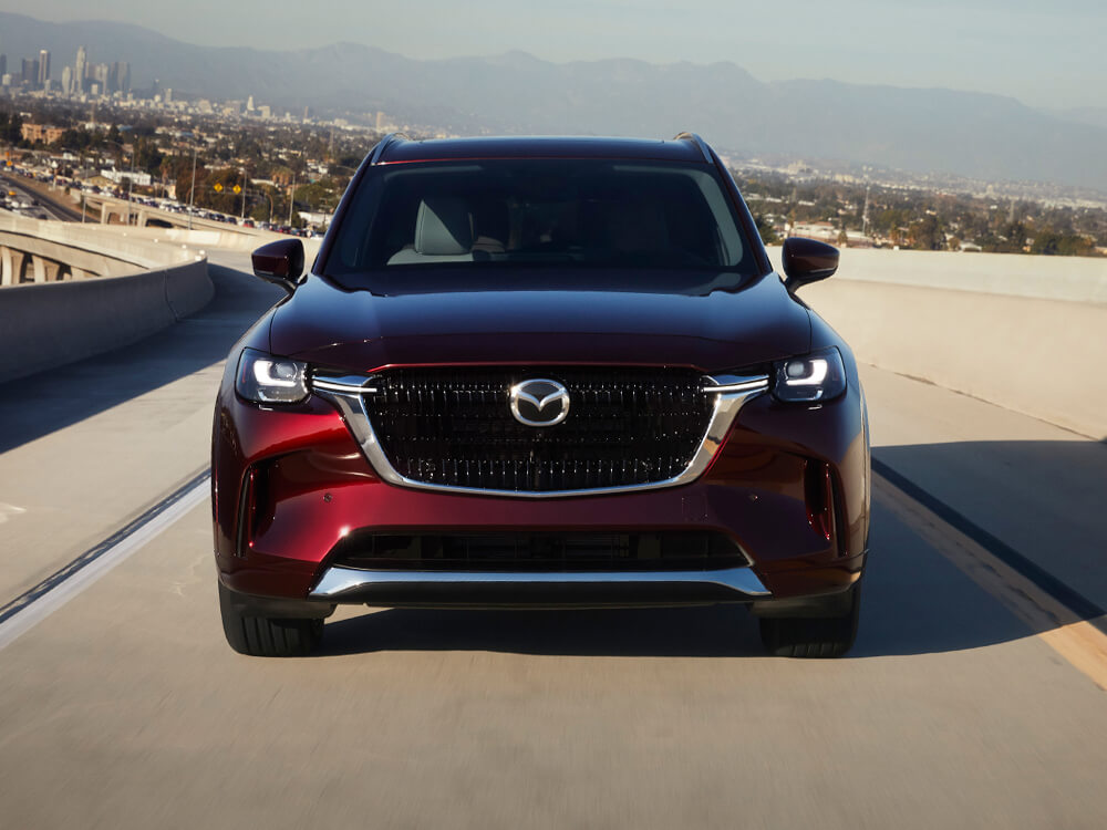 Gros plan d’un CX-90 rouge artisan qui roule vers la caméra sur un viaduc en béton.