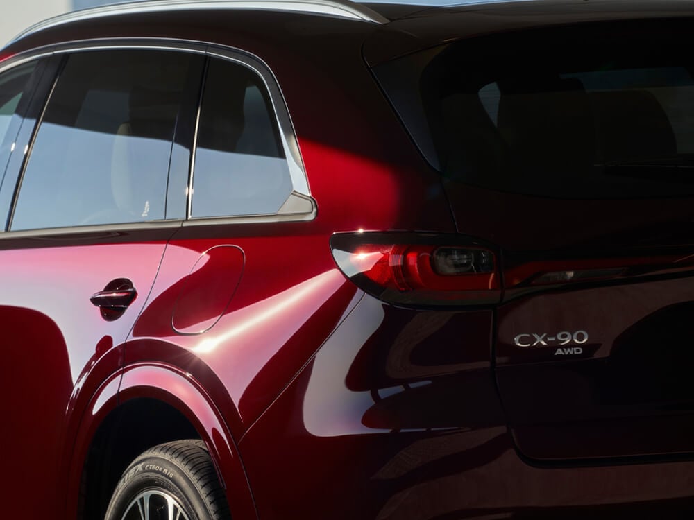 Le soleil brille sur le passage de la roue et du feu arrière gauche d’un CX-90 rouge artisan.  