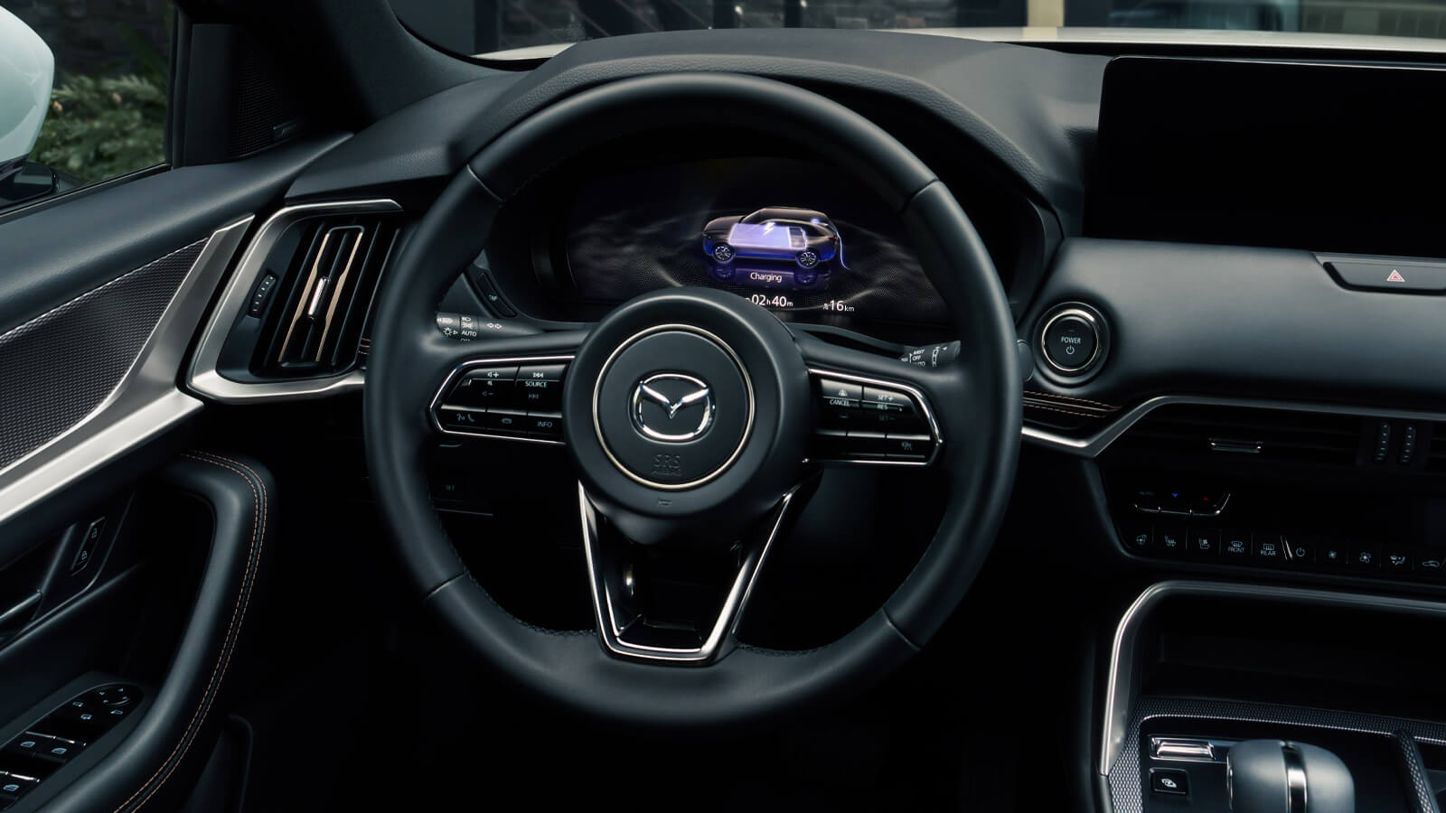 Close up of steering wheel and dash display beyond. The display shows the charge level of the CX-90 as it is charging. 