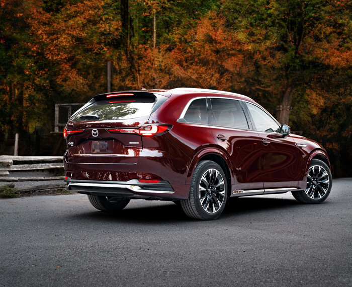 Sunlight gleaming off of the back left wheel well and taillight of an Artisan Red CX-90.