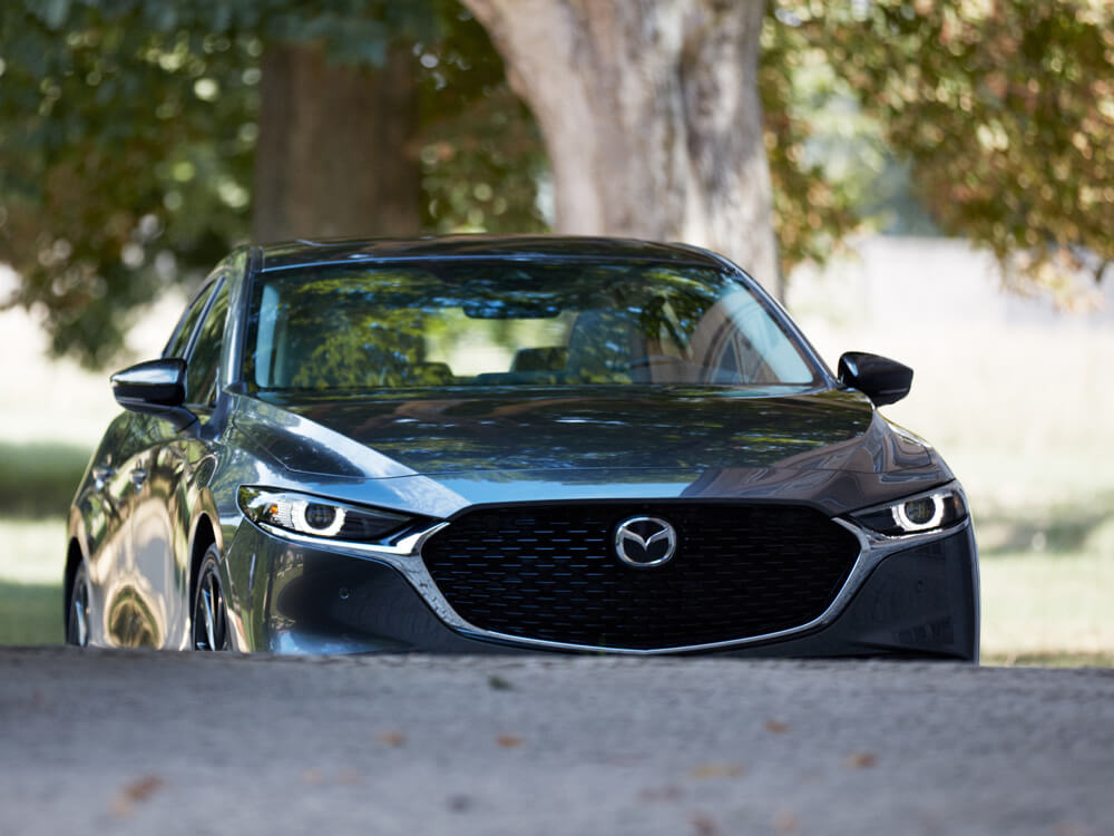 Front of the Mazda3 sedan approaching an inclined driveway.   