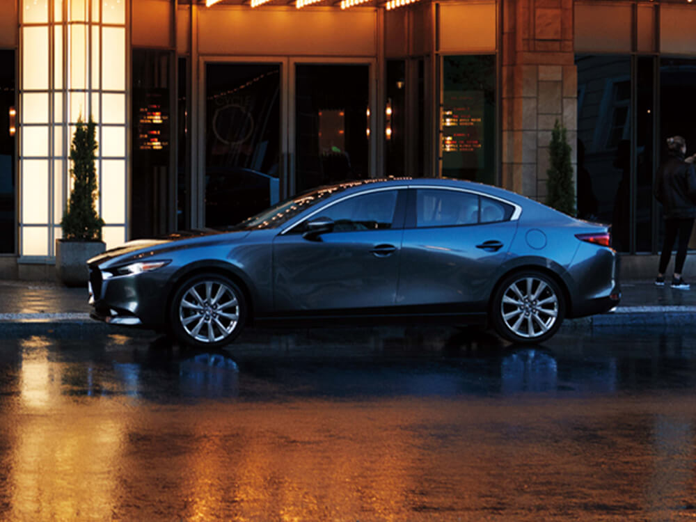 Mazda3 Sedan parked in front of shop entrance on city street. 