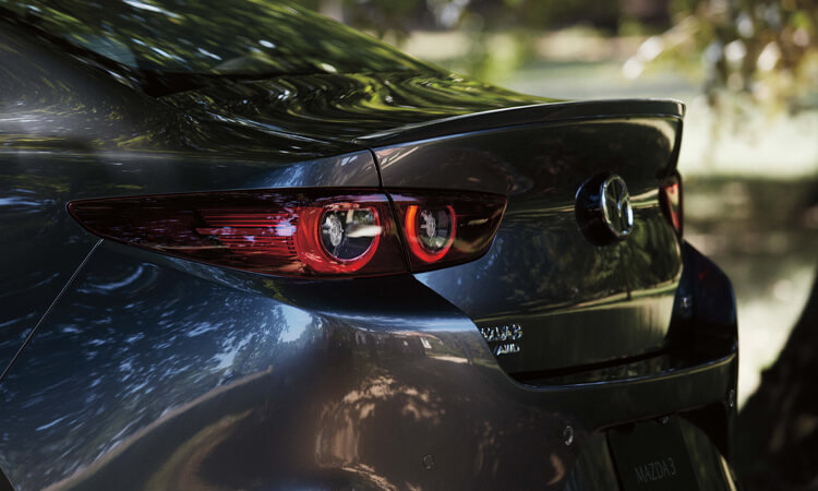 Close-up of Machine Grey Metallic Mazda3 sedan rear profile. 