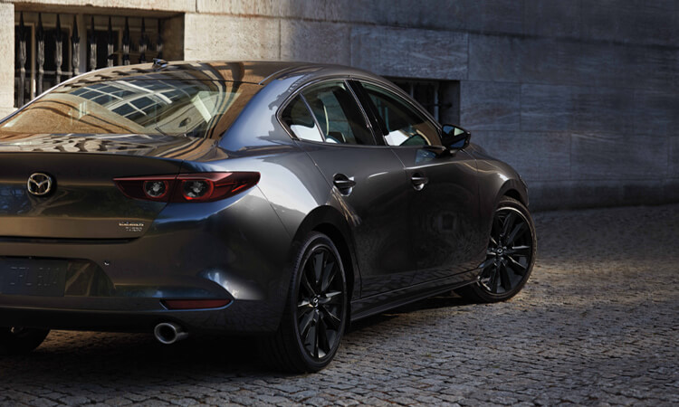 Mazda3 sedan making a tight left turn down a steep cobblestone pathway.