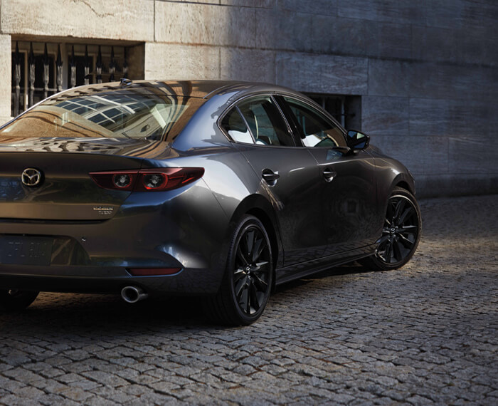 Mazda3 sedan making a tight left turn down a steep cobblestone pathway.