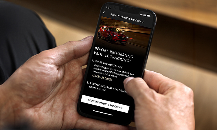 Hands holding smartphone with Mazda Stolen Vehicle Tracking on screen 
