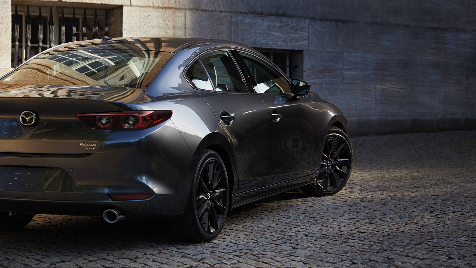 A platinum Mazda3 parked on the street.