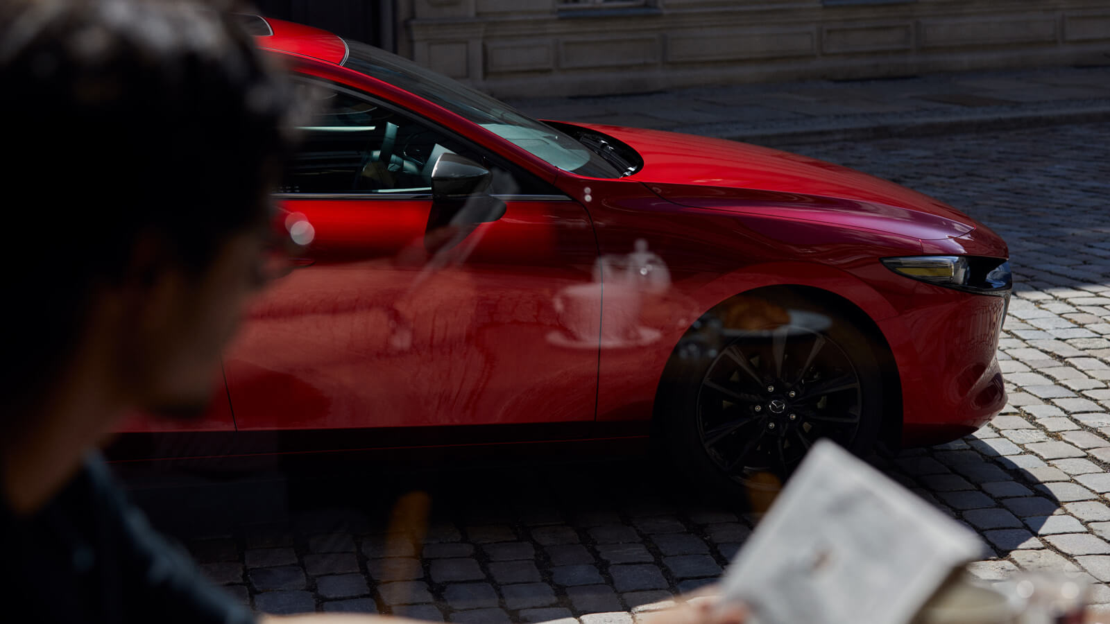 Close-up of nose profile of Soul Red Crystal Metallic Mazda3 Sport parked on cobblestone street. 