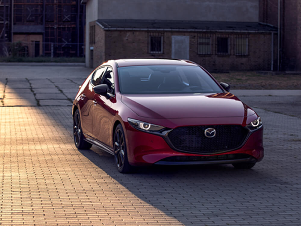 Soul Red Crystal Metallic Mazda3 Sport parked in front of main street shop at sundown.  