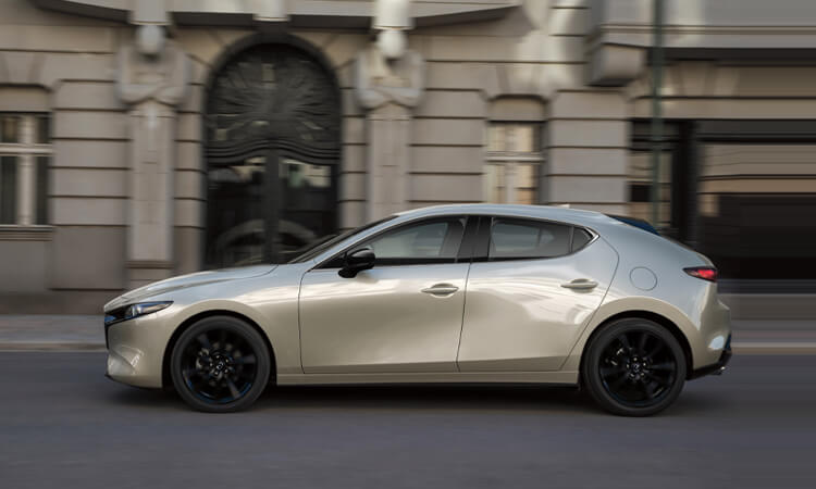 Mazda3 Sport drives down city street, passing a hotel’s large arched entryway. 