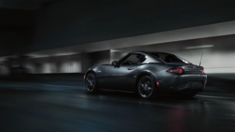 Une MX-5 RF sombre roule sur une route urbaine la nuit. 