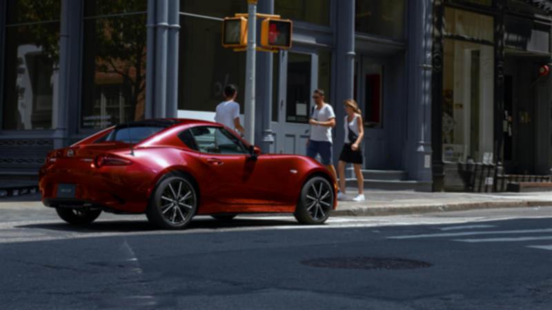 Une MX-5 RF rouge roule dans une rue urbaine le jour. 