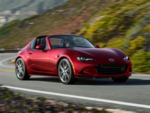 Une MX-5 RF rouge roule sur une route sinueuse avec un paysage flou en arrière-plan.  