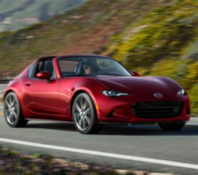 Une MX-5 RF rouge roule sur une route sinueuse bordée de collines. 