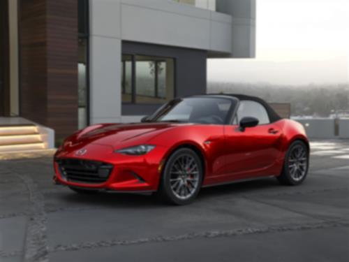 3/4ths view of a red MX-5 ST parked in front of a modern home with its top up.